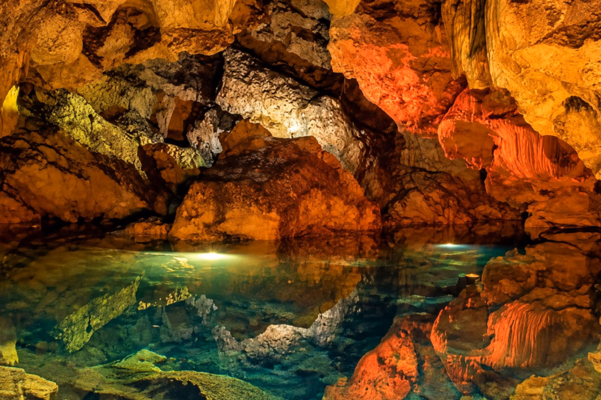Underground lake lit in orange and green inside Green Grotto Caves