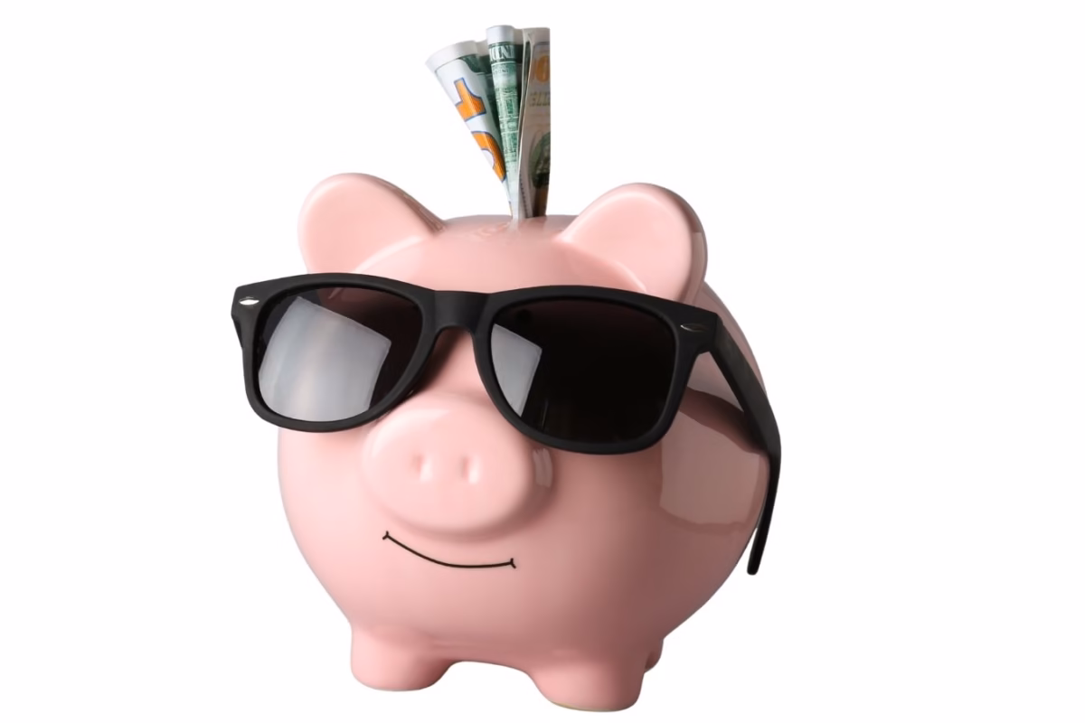 Pink piggy bank wearing sunglasses with dollar bills in the slot