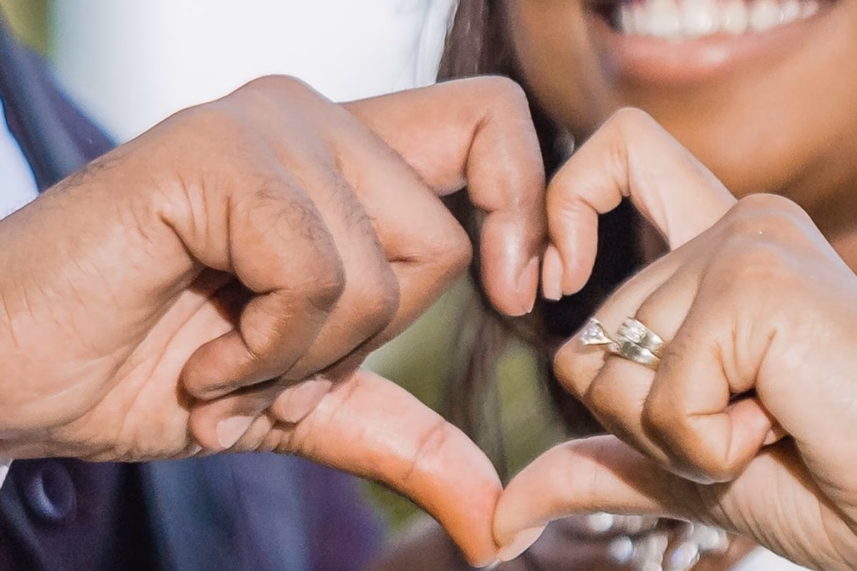 Couple making a heart shape with their hands, showing an engagement ring
