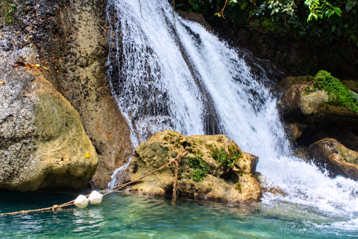 Waterfall tumbling over boulders into a clear green pool at Reach Falls